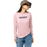 Person wearing a pink long-sleeve shirt with 'EXPLORE MORE' text, blue jeans, and a brown hat on a white background