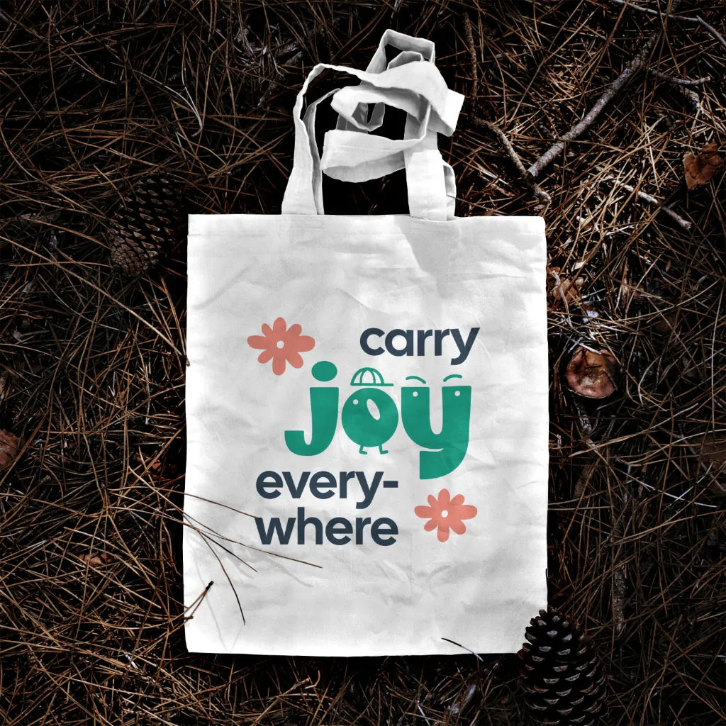 Tote bag with 'carry joy everywhere' text on a natural background