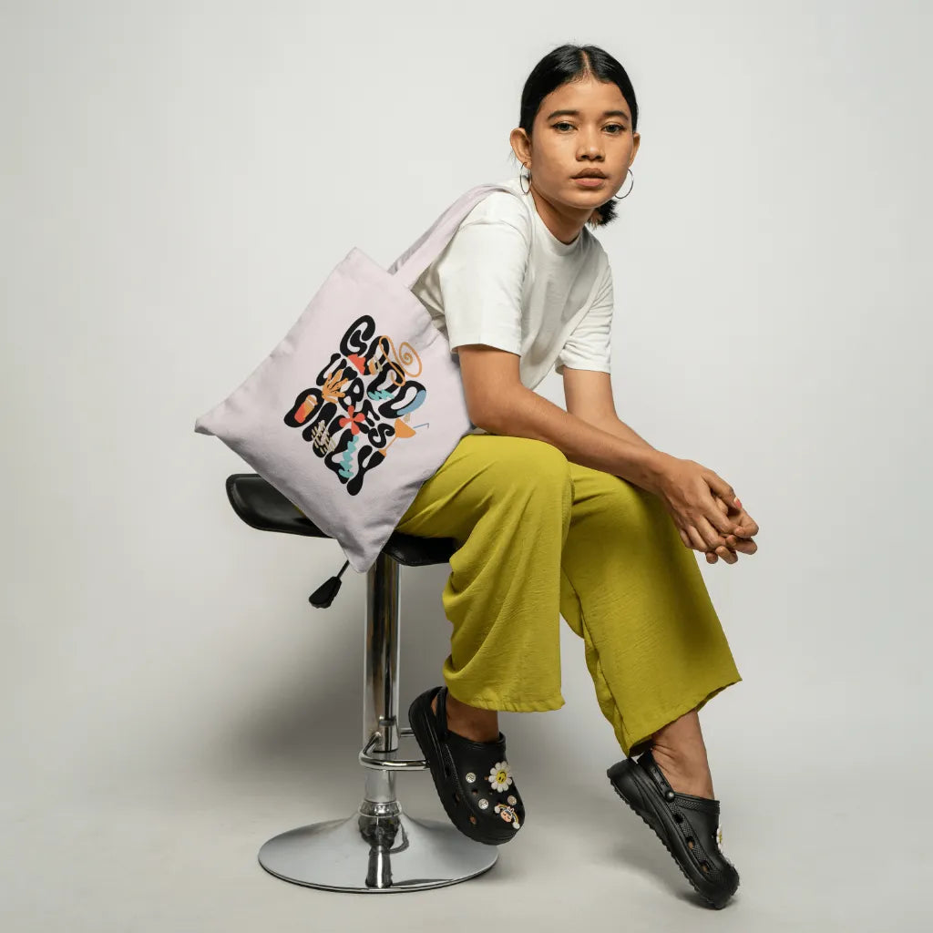 Person sitting on a stool with a tote bag featuring colorful text.