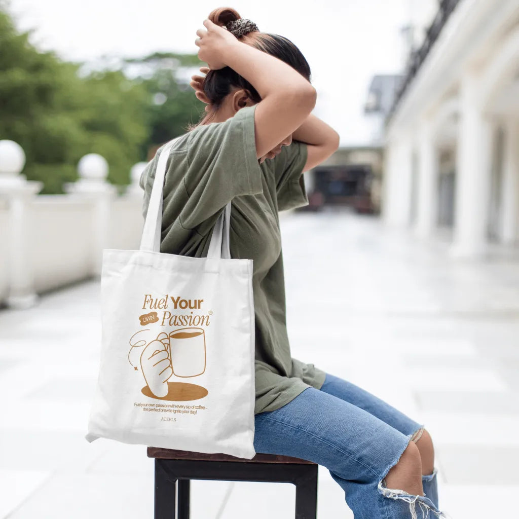 Person sitting outdoors with a tote bag featuring 'Fuel Your Passion' text and graphic.