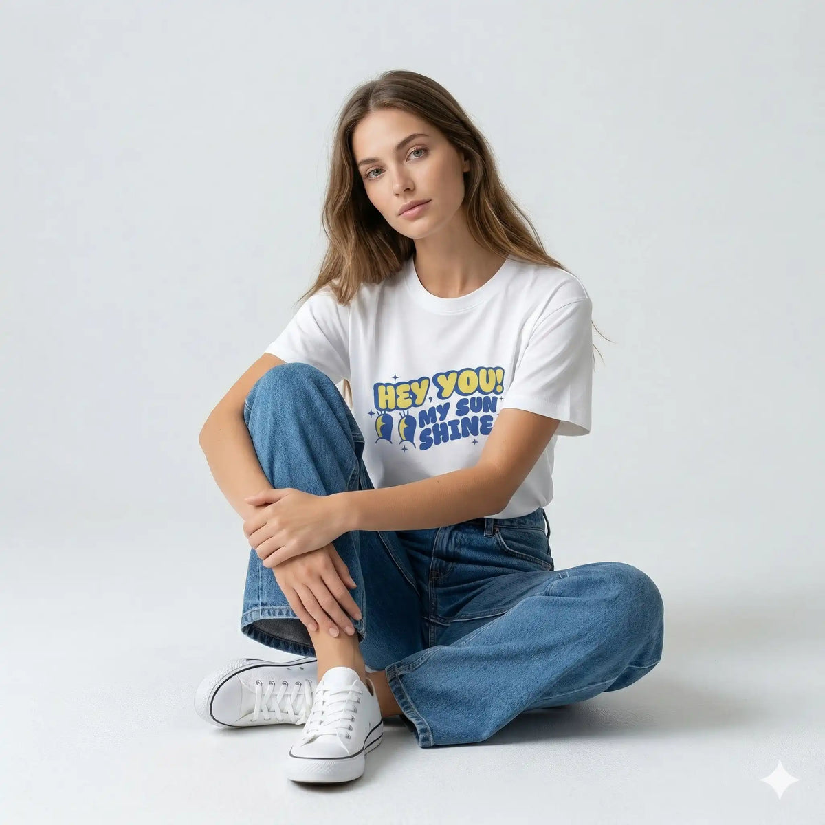 Woman wearing a white t-shirt with text and blue jeans sitting on a light gray background