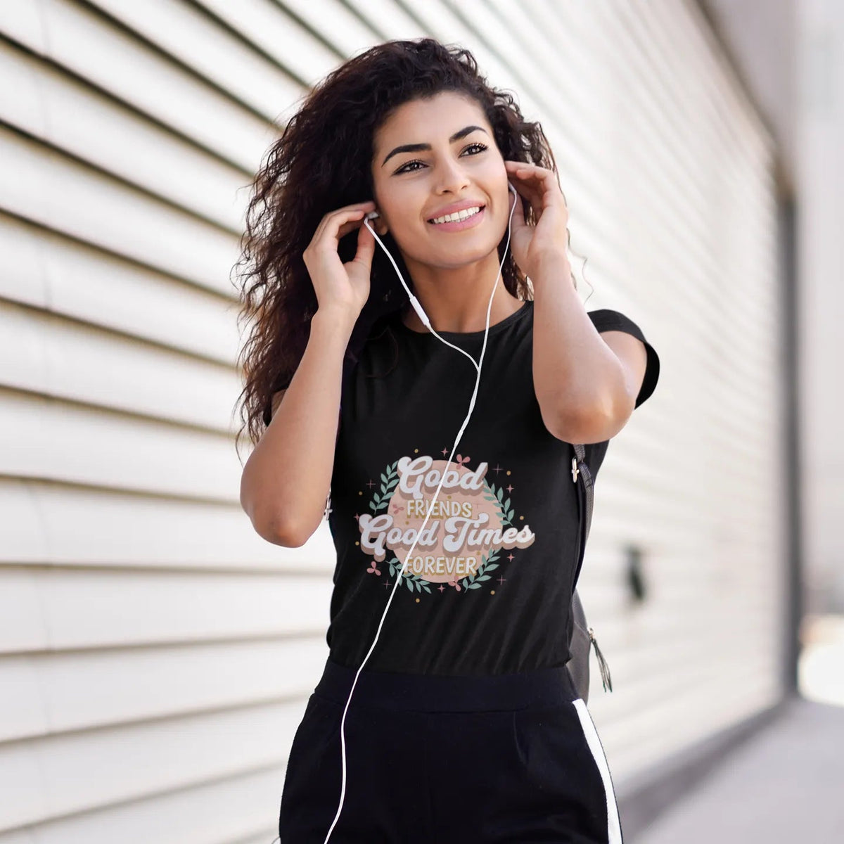 Woman wearing a black t-shirt with text and headphones, standing against a light-colored wall.