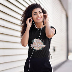 Woman wearing a black t-shirt with text and headphones, standing against a light-colored wall.