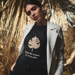 Woman wearing a black t-shirt with a leaf design and text, standing against a gold leafy background.