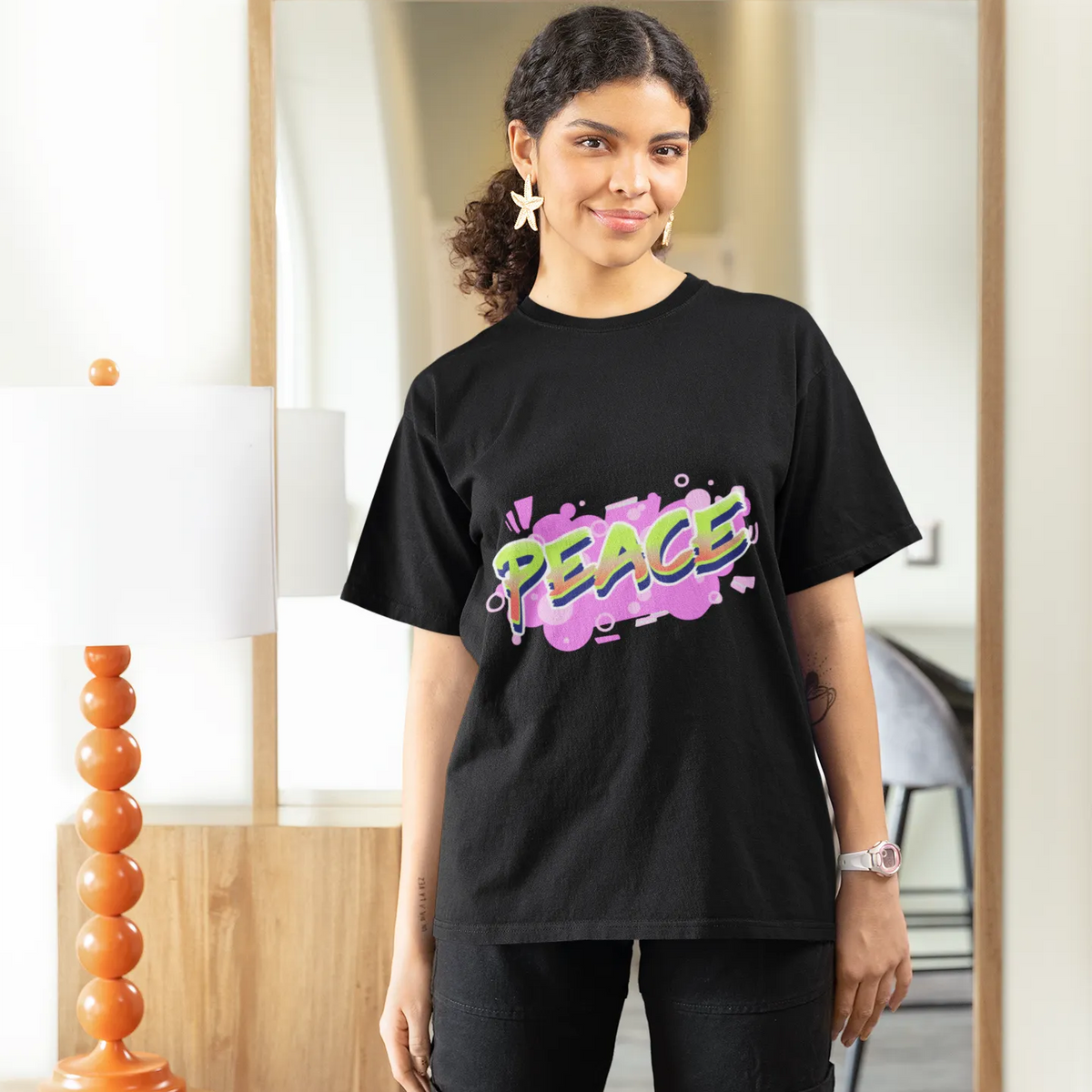 Person wearing a black t-shirt with colorful text, standing in a room.