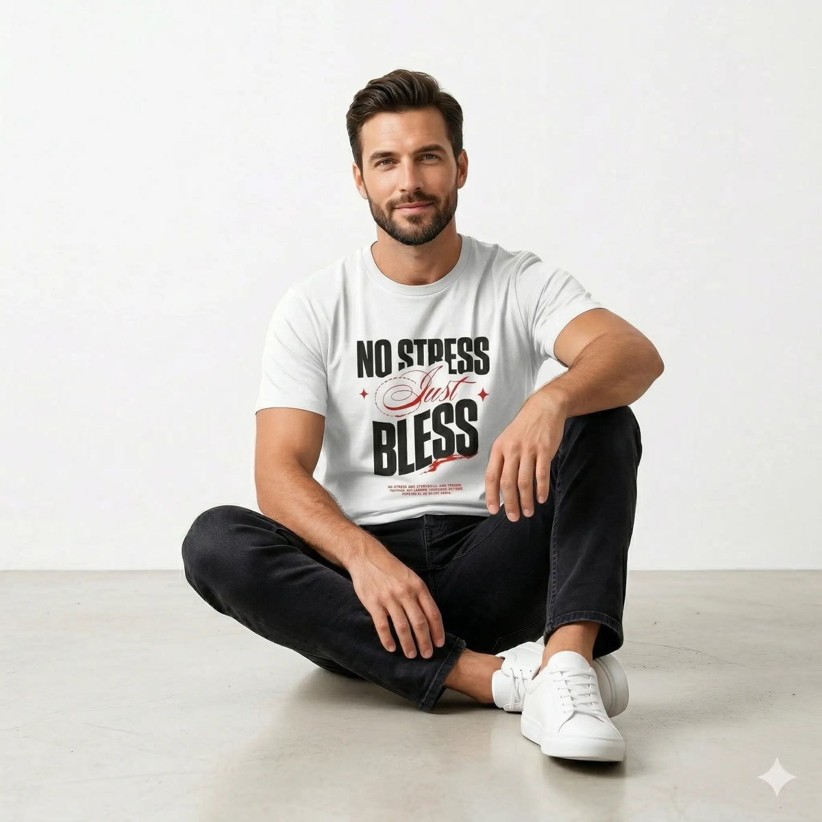 Man sitting on the floor wearing a white t-shirt with text, sitting against a plain background.