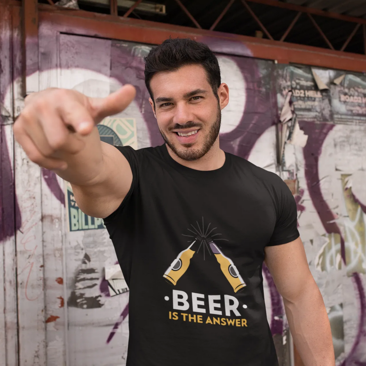 Man wearing a black t-shirt with 'Beer is the Answer' design, pointing forward against a graffiti-covered wall.