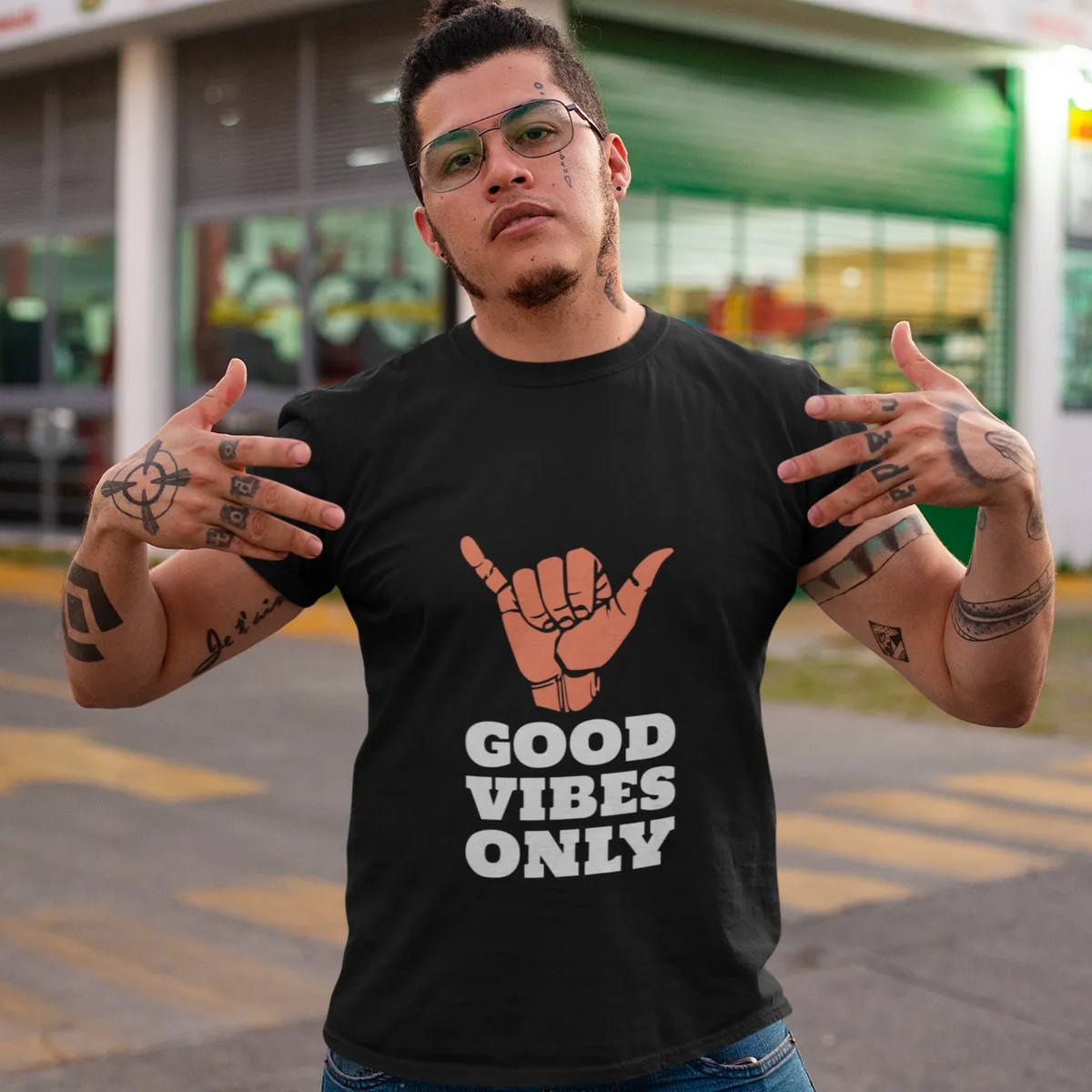 Person wearing a black t-shirt with 'Good Vibes Only' text and a hand sign, standing outdoors.