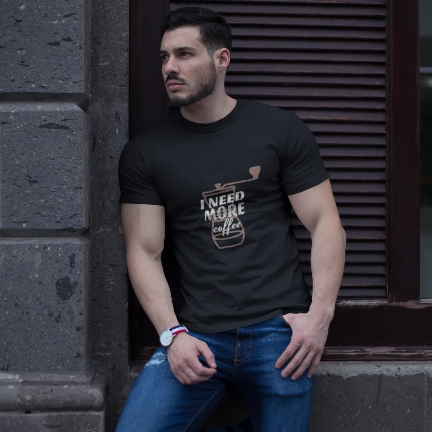 Man wearing a black t-shirt with text and graphics, leaning against a stone wall.