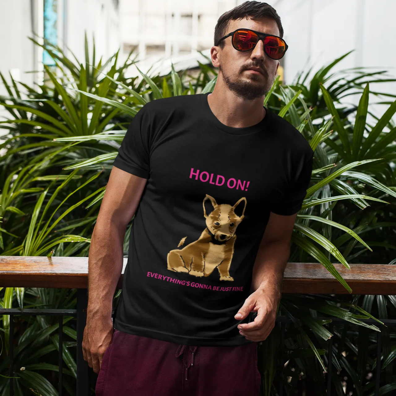 Man wearing a black t-shirt with a graphic and text, standing in front of green plants.