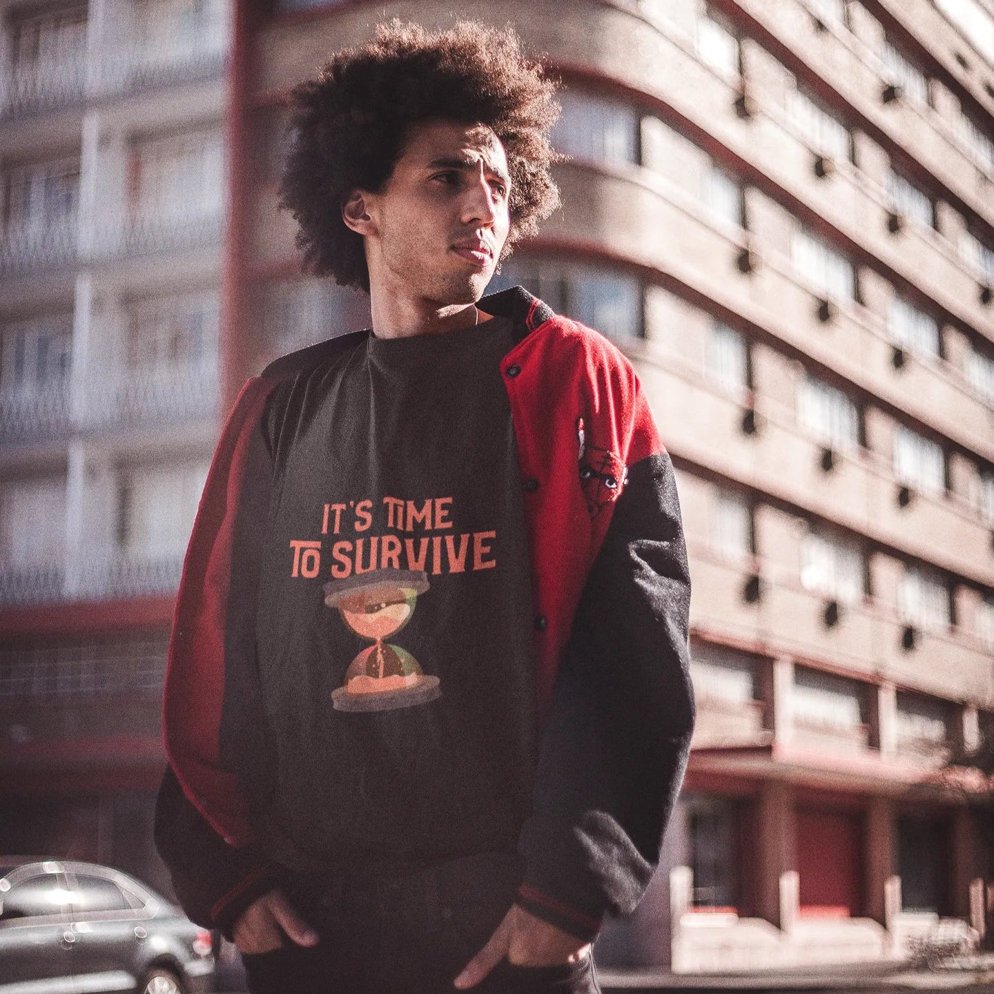 Person wearing a black and red jacket with text and graphic design, standing in front of a building.