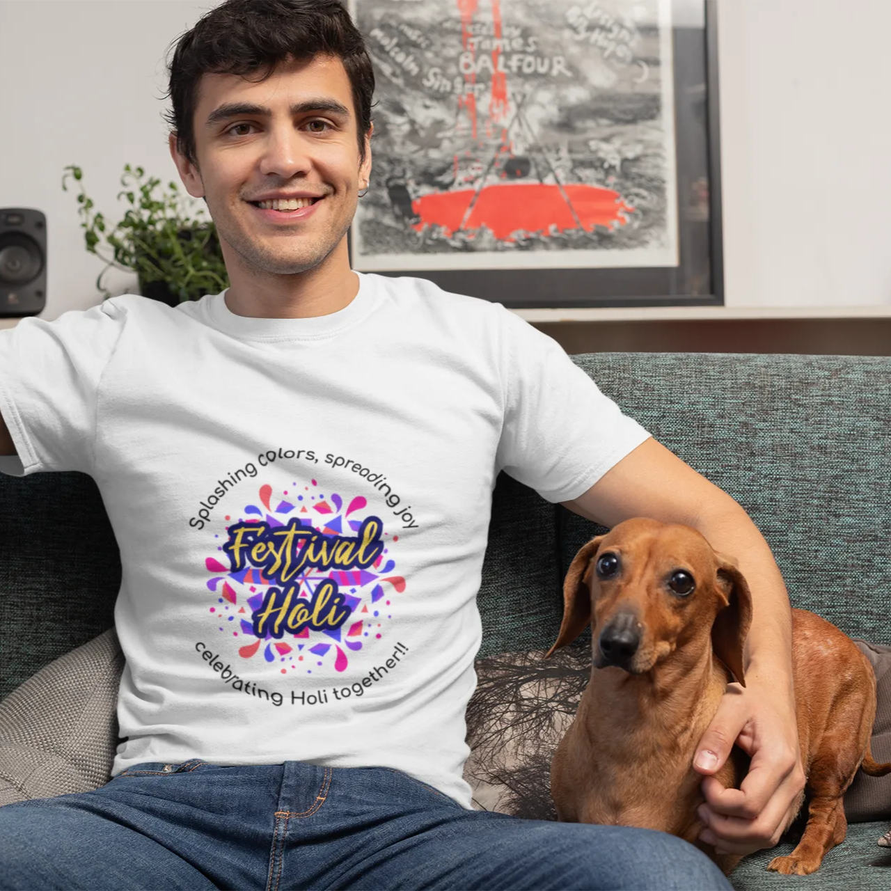 Man wearing a white t-shirt with a colorful design, sitting on a couch with a dog.