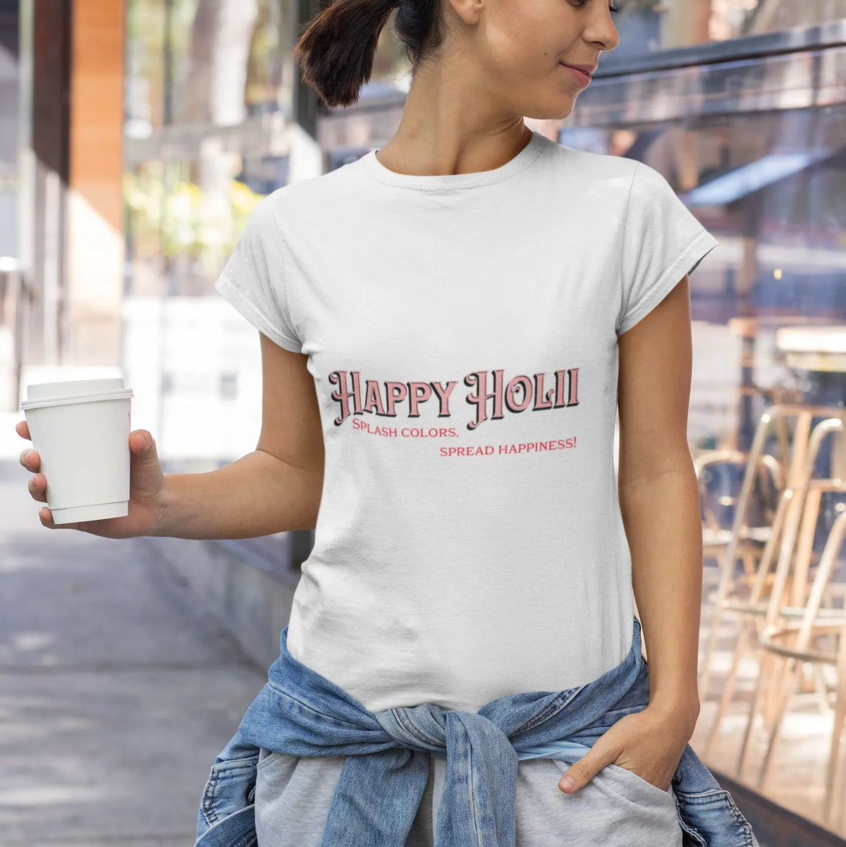Woman wearing a white t-shirt with 'Happy Holly' text, holding a cup outdoors.