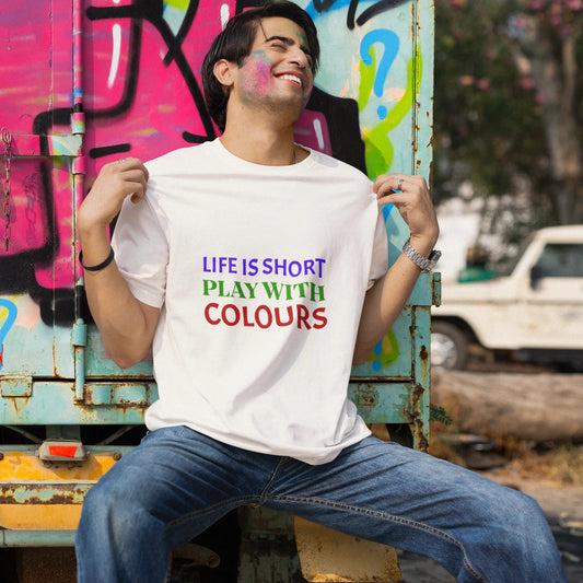 Person wearing a white t-shirt with colorful text, sitting against a graffiti-covered wall.