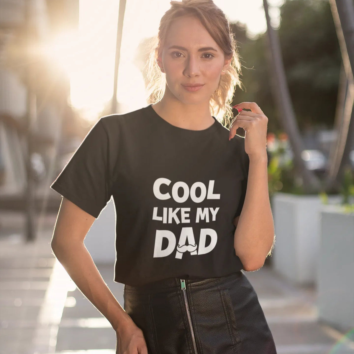 Woman wearing a black t-shirt with 'Cool like my dad' text outdoors.