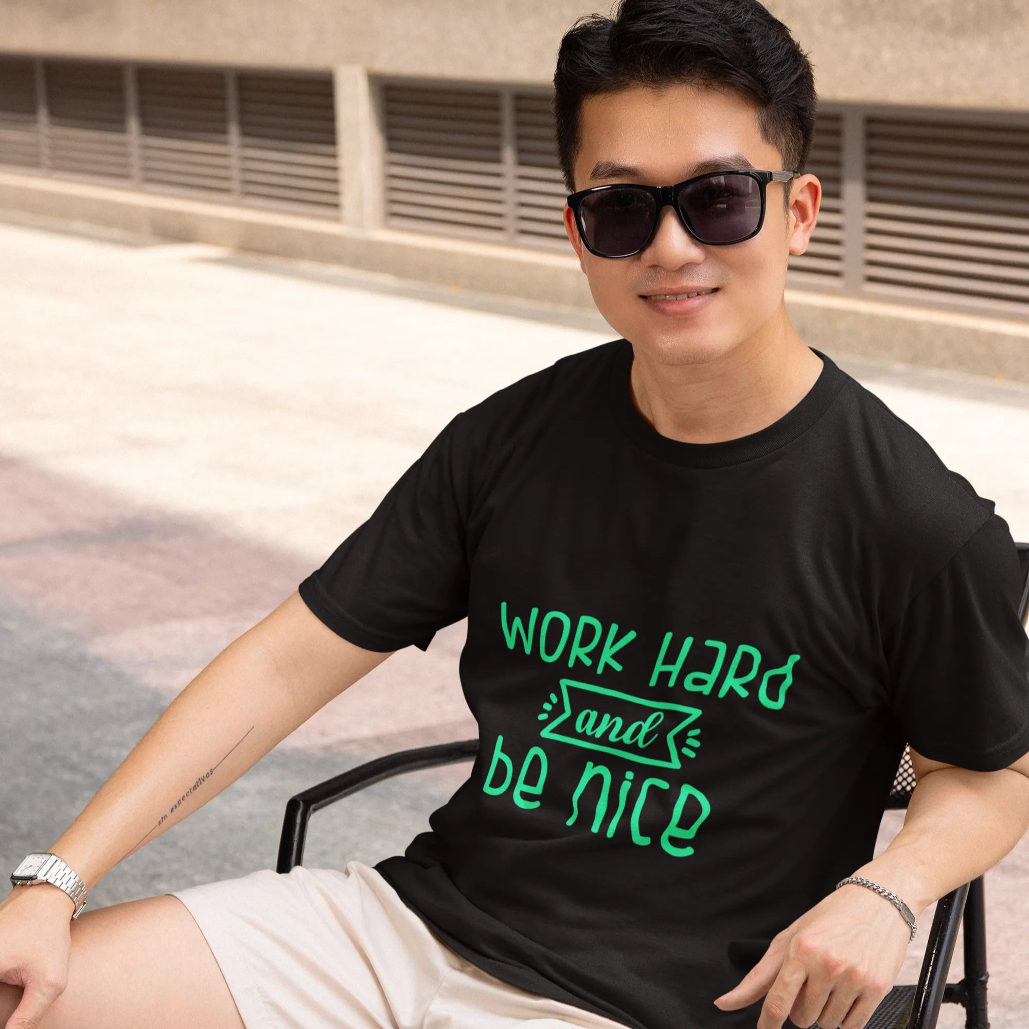 Person wearing a black t-shirt with 'Work Hard and Be Nice' text, sitting outdoors.
