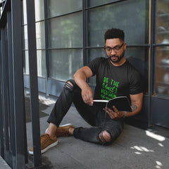 Man sitting on a sidewalk reading a book with a modern building in the background