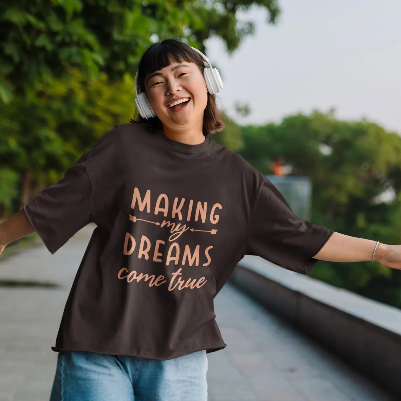 Person wearing a black sweatshirt with 'Making my dreams come true' text, standing outdoors with arms outstretched.