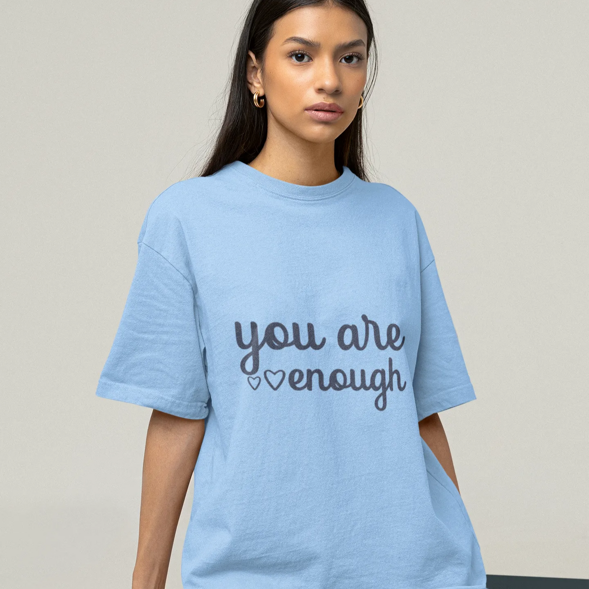 Person wearing a light blue t-shirt with 'you are enough' text on a plain background