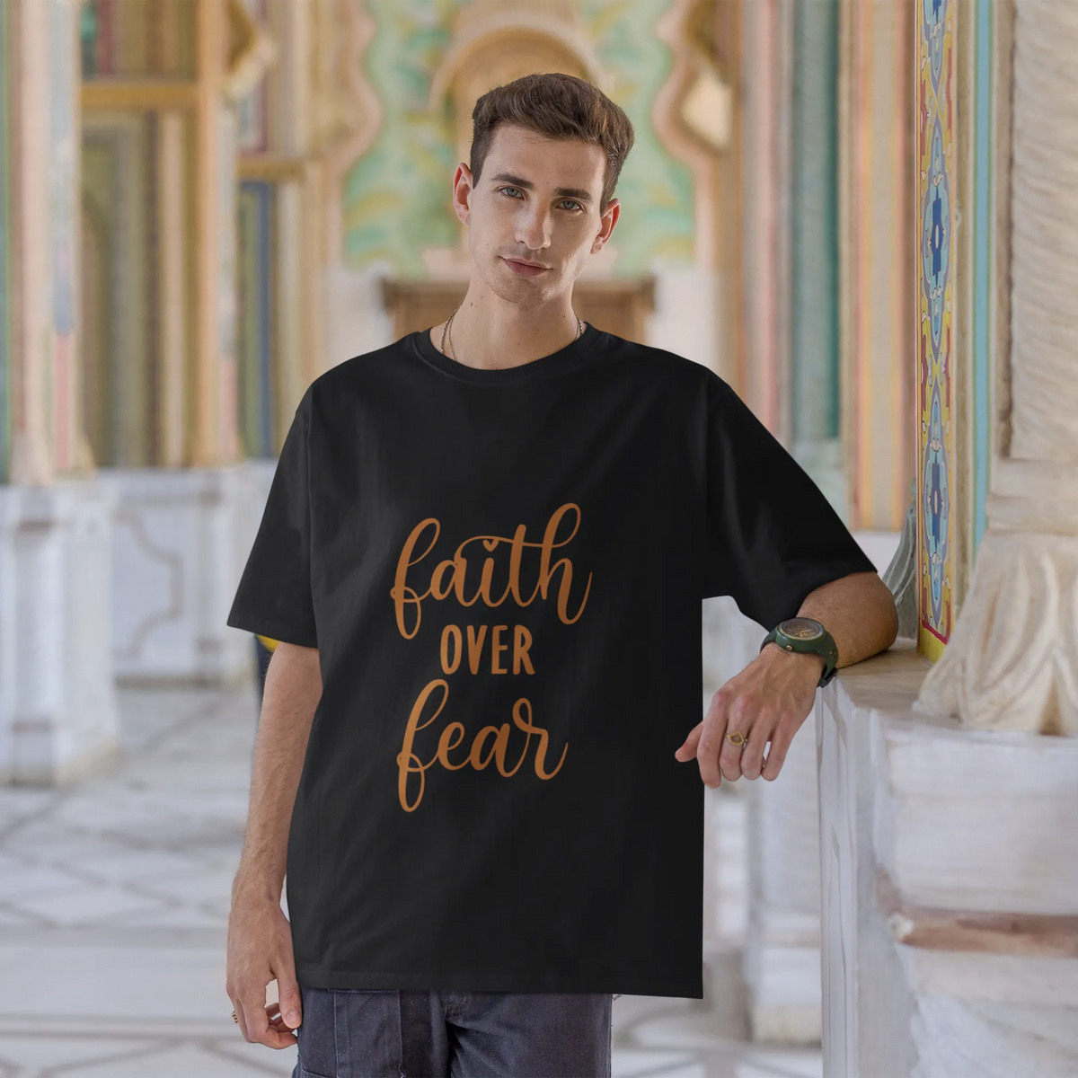 Man wearing a black t-shirt with 'faith over fear' text in an ornate architectural setting.