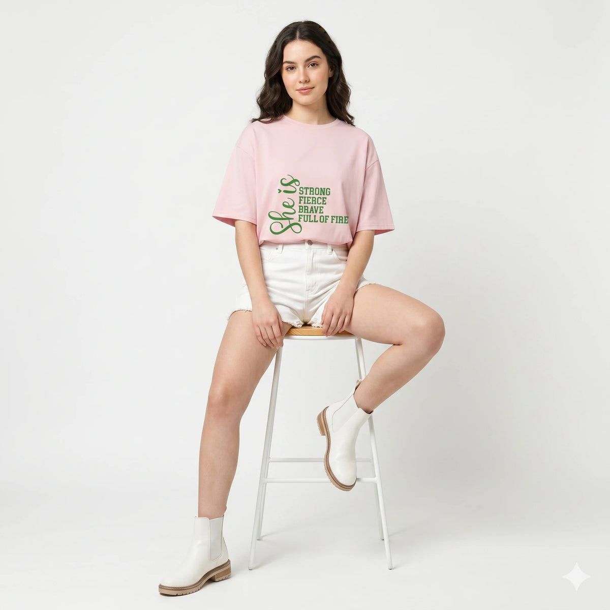 Woman sitting on a stool wearing a pink t-shirt with text and white shorts on a light gray background