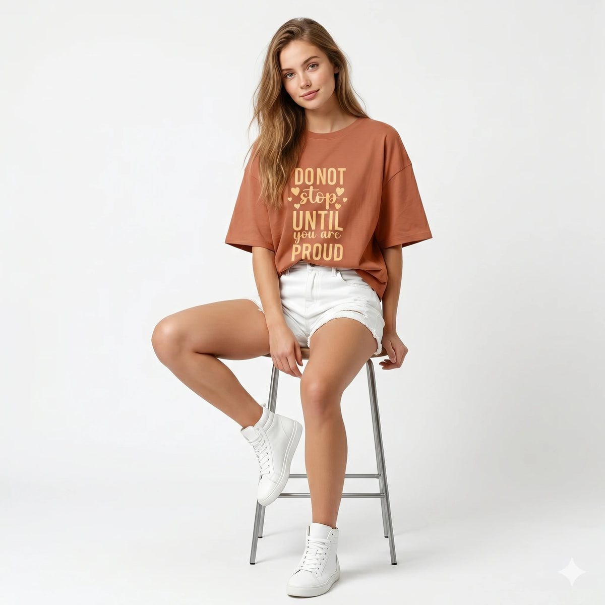 Brown t-shirt with 'Do not stop until you are proud' text on a hanger against a gray concrete wall.