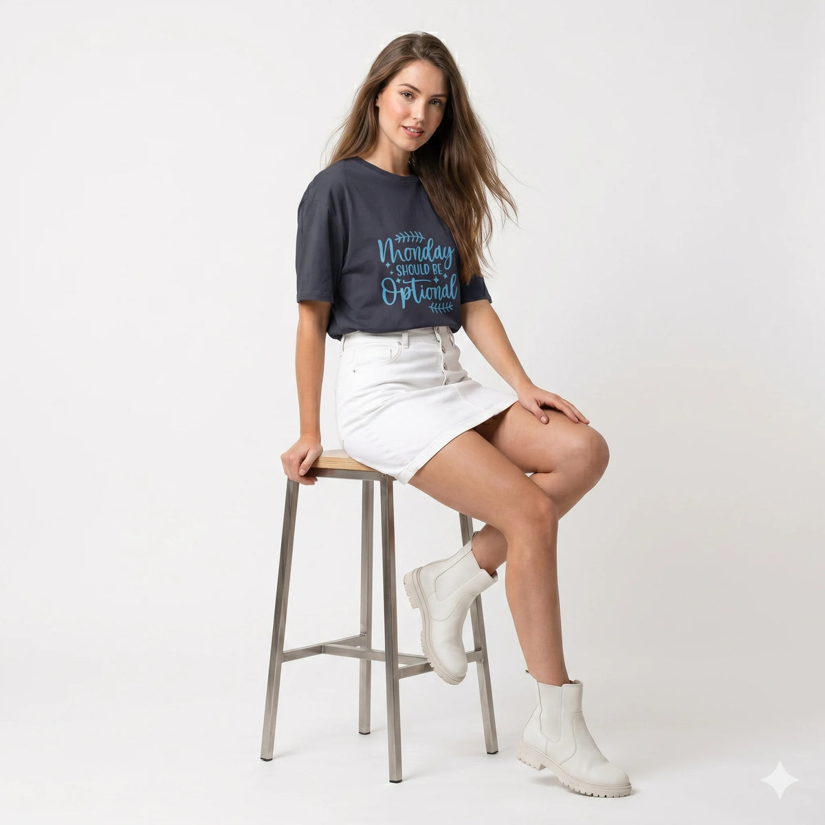 Woman sitting on a stool wearing a dark blue t-shirt with text, white skirt, and white boots on a light gray background.