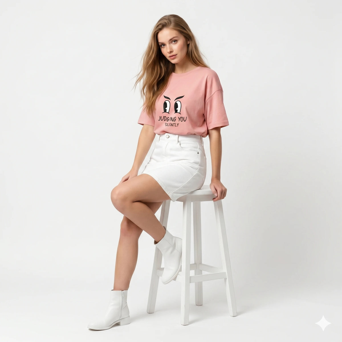 Woman wearing a pink graphic t-shirt and white shorts sitting on a stool against a white background