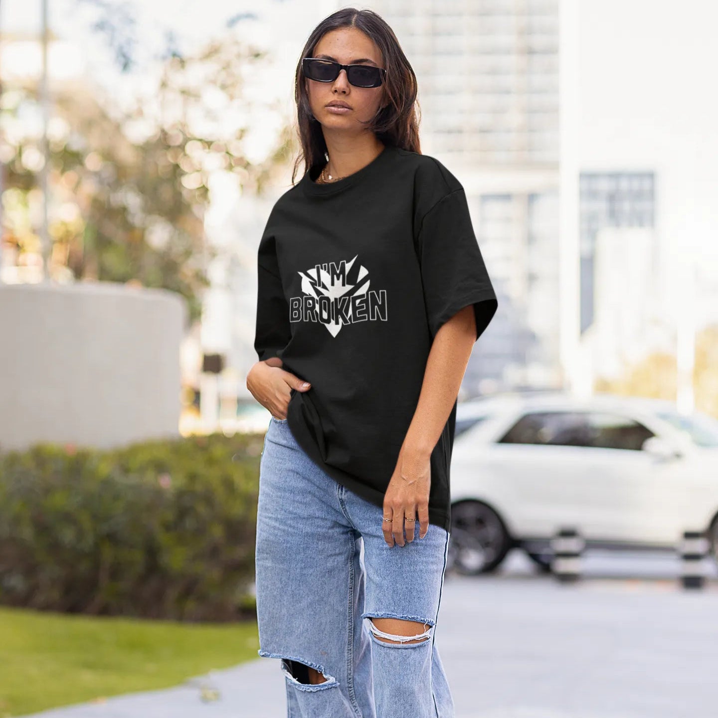 Woman wearing a black t-shirt and ripped jeans standing on a sidewalk.