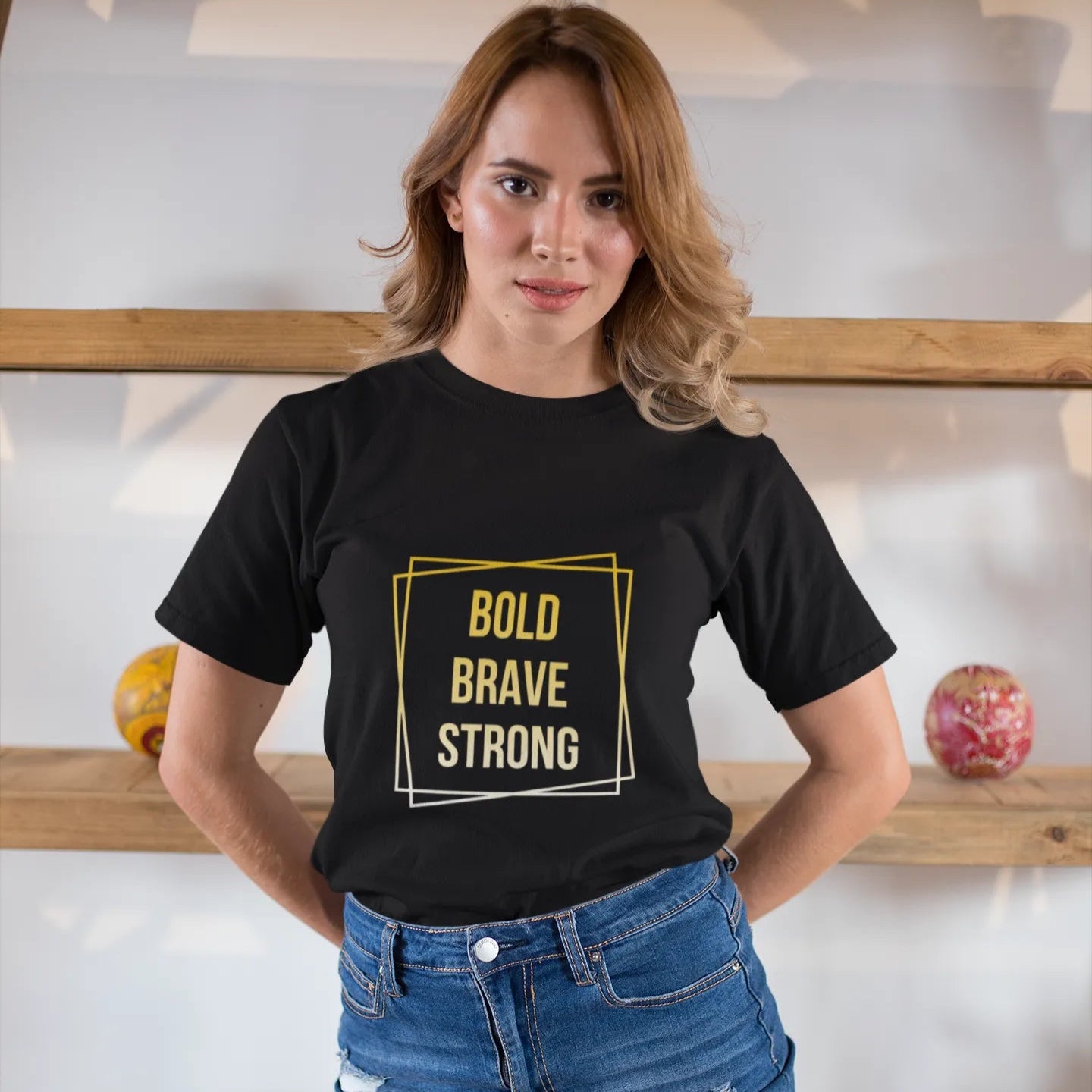Woman wearing a black t-shirt with 'Bold Brave Strong' text in a yellow box, standing indoors.