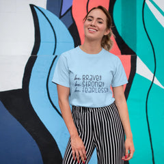 Woman wearing a light blue t-shirt with motivational text in front of a colorful mural.