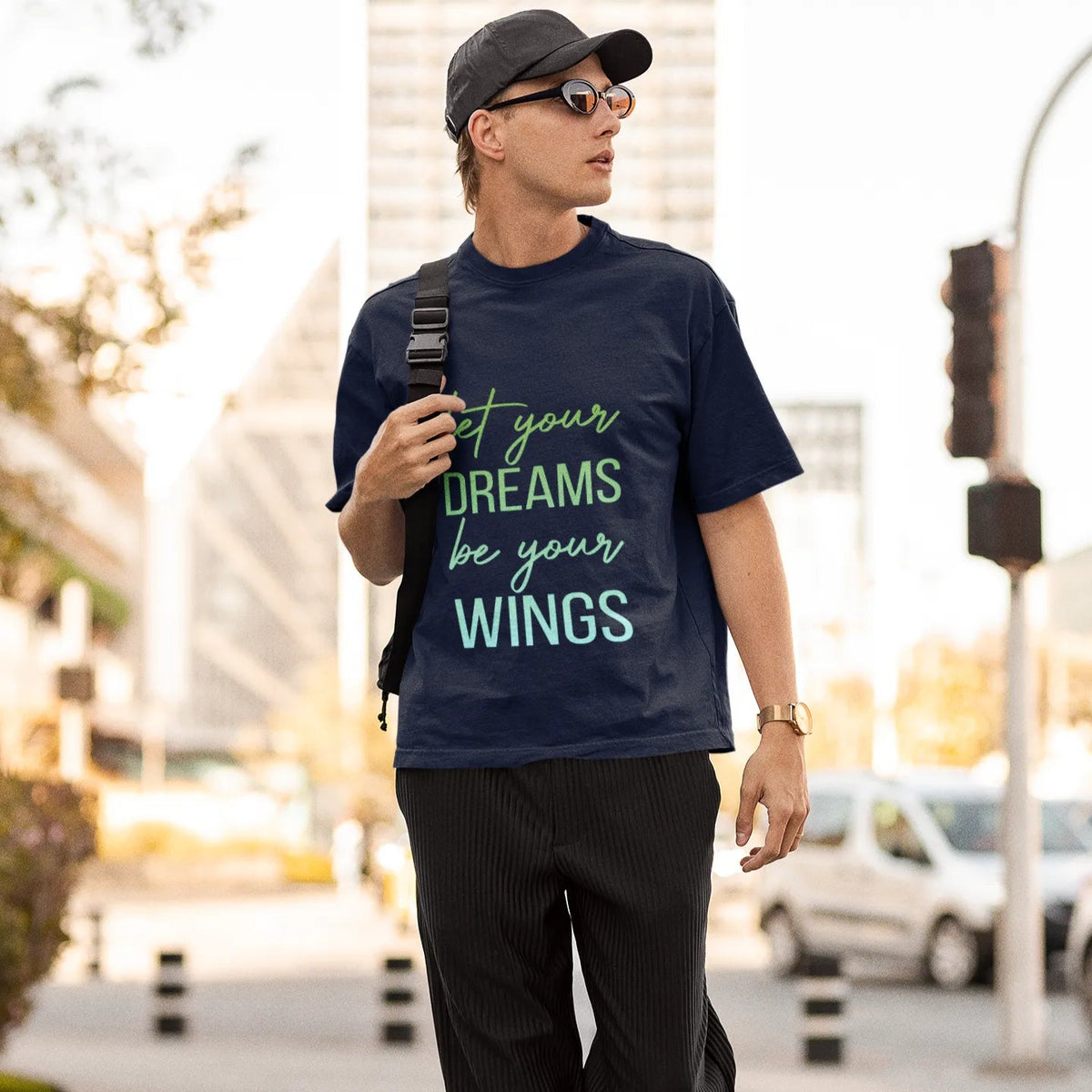 Man walking outdoors wearing a navy t-shirt with motivational quote, black pants, and cap.