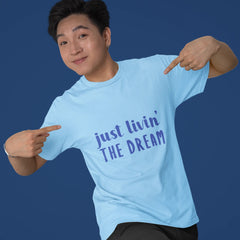 Person wearing a light blue t-shirt with 'just livin' THE DREAM' text on a solid background