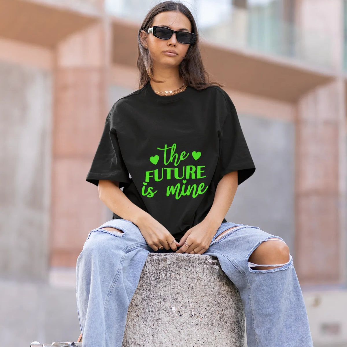 Person wearing a black t-shirt with 'The Future is Mine' text, sitting on a concrete block outdoors.