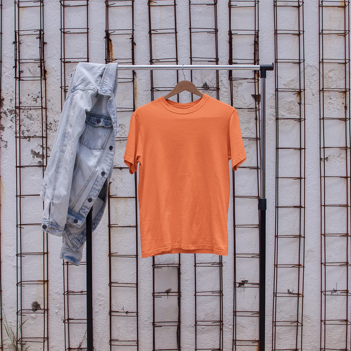 Orange t-shirt on a rack with denim jacket and white sneakers in front of a textured wall.