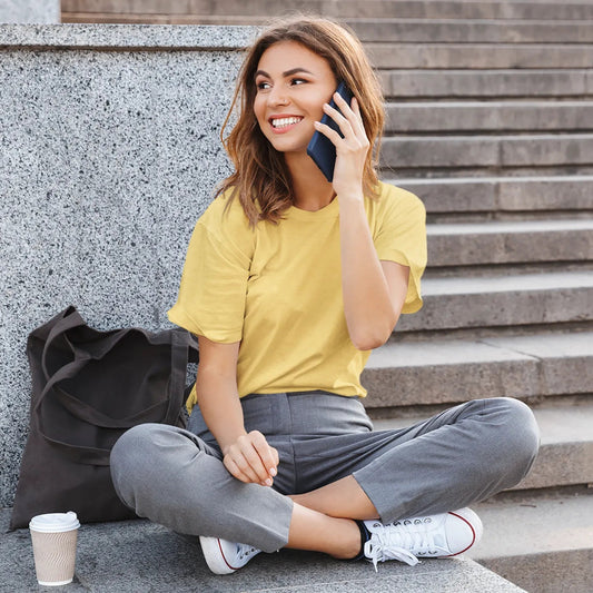 Woman sitting on steps talking on a phone with a coffee cup nearby