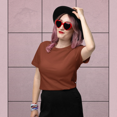 Person wearing a brown shirt and black shorts with heart-shaped sunglasses against a pink tiled wall.