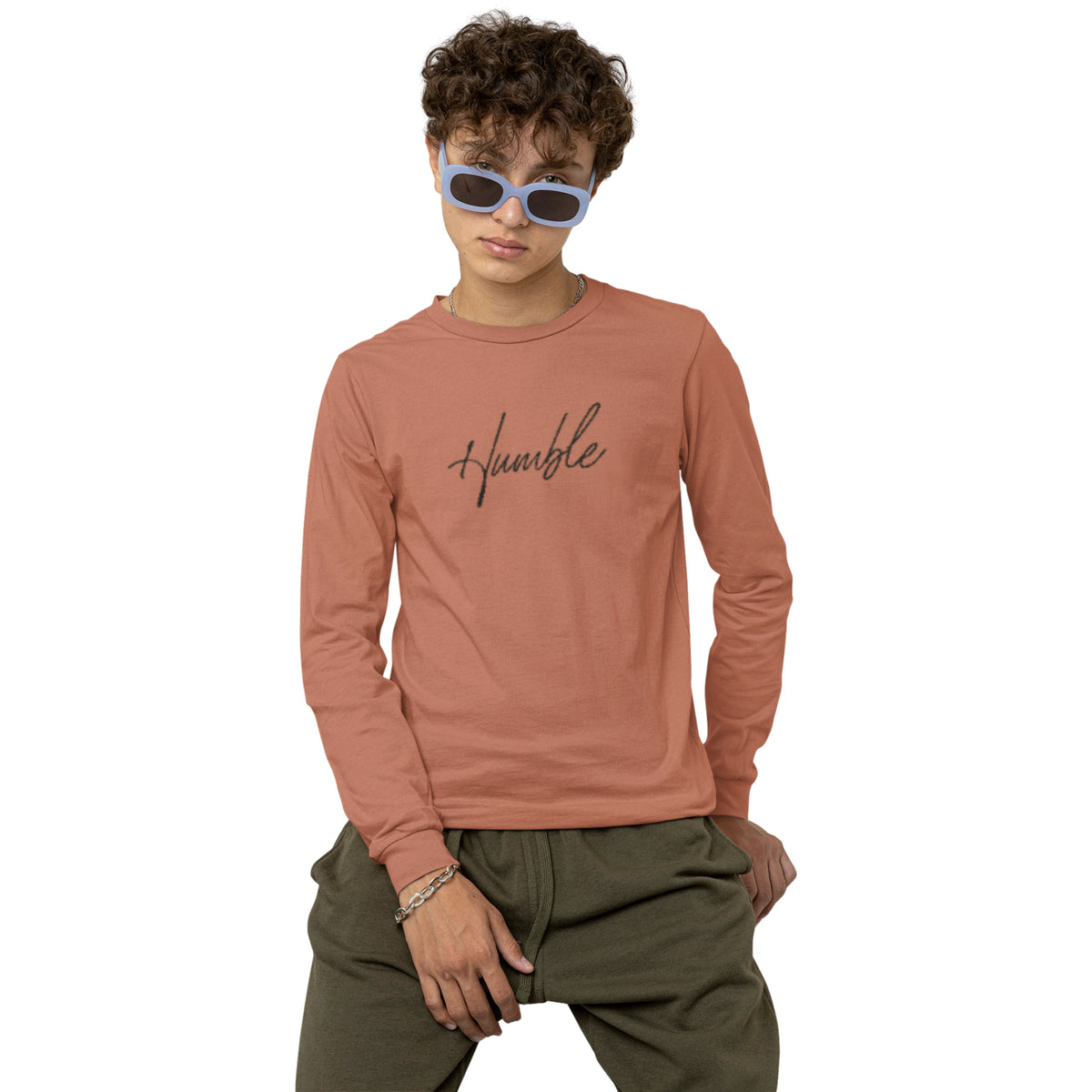 Person wearing a pink long-sleeve shirt with 'humble' text and green pants on a white background