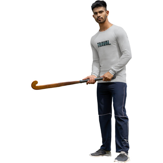 Man holding a hockey stick wearing a gray 'TRAVAL' shirt and navy pants on a white background