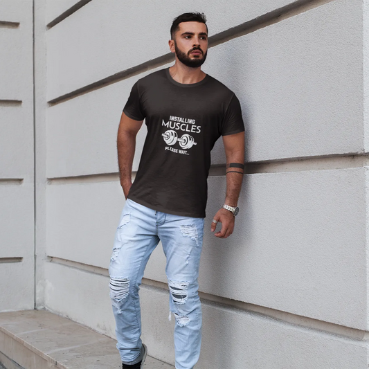 Man wearing a black t-shirt with text and light blue jeans standing against a white wall.