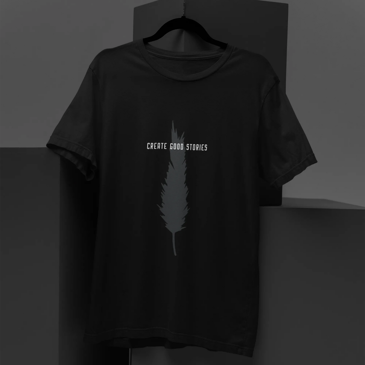 Black t-shirt with feather graphic and 'Create Good Stories' text on a dark background