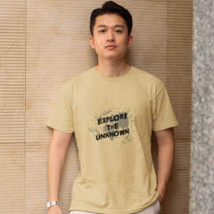 Man wearing a light green t-shirt with 'Explore the Unknown' text against a textured wall.