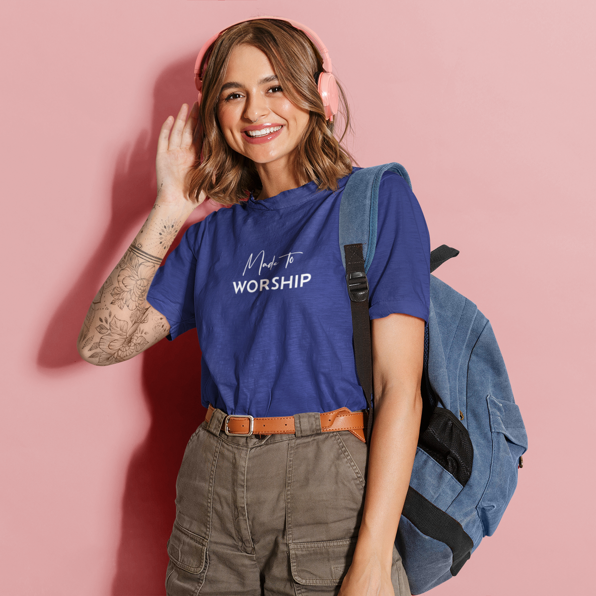 Woman wearing a blue t-shirt with text, holding a backpack against a pink background