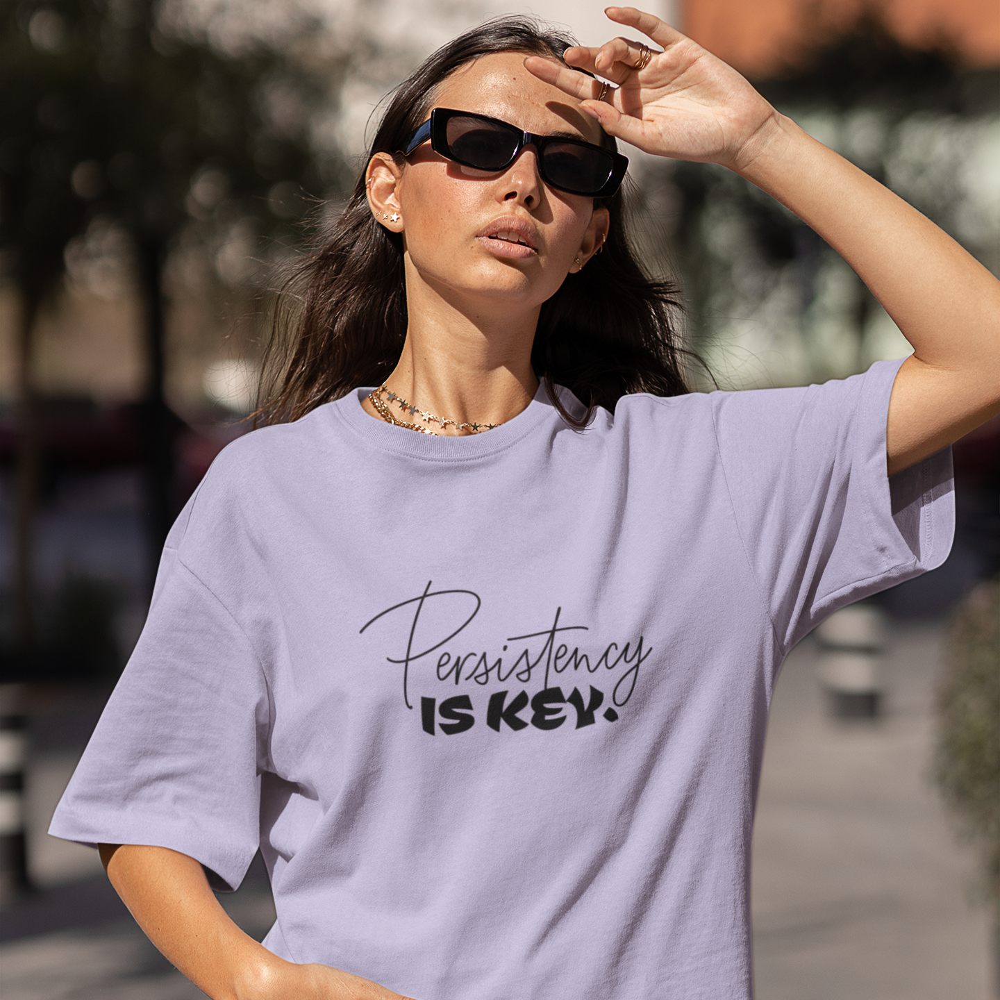 Woman wearing a lavender t-shirt with 'Persistence is Key' text outdoors.
