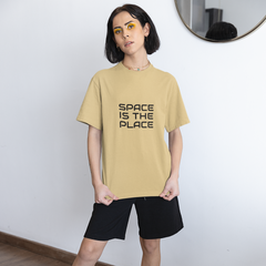 Person wearing a beige t-shirt with 'Space is the Place' text, black shorts, and white sneakers in a room.