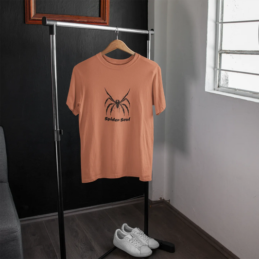 Peach t-shirt with a spider graphic on a hanger in a room with a window.