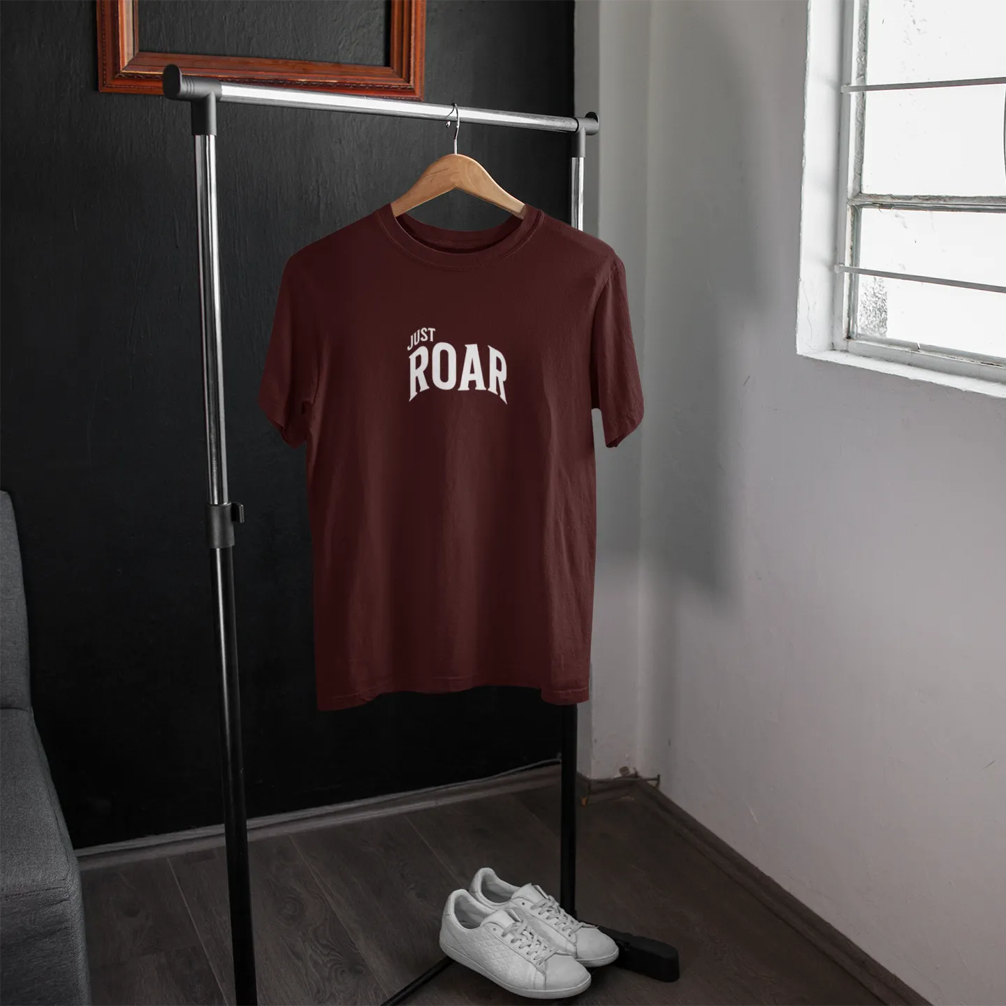 Brown t-shirt with 'JUST ROAR' text on a hanger in a room with a window.
