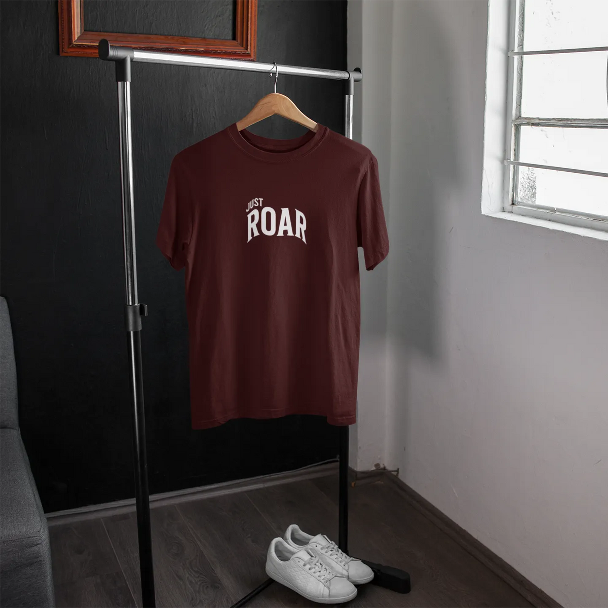 Brown t-shirt with 'JUST ROAR' text on a hanger in a room with a window.