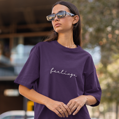 Woman wearing a purple t-shirt with 'feelings' text outdoors.