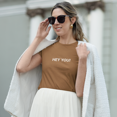 Woman wearing a brown t-shirt with 'HEY YOU!' text outdoors.